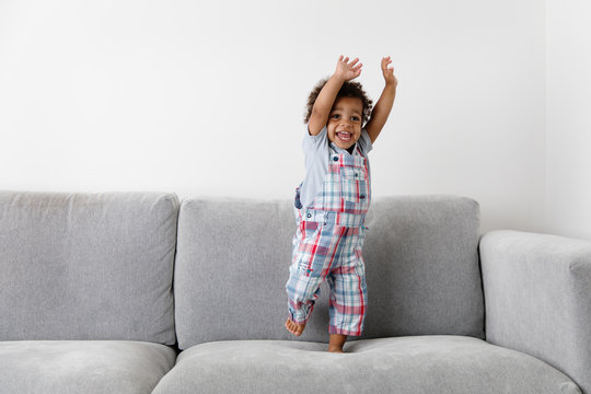 laughing toddler standing on couch raising hands