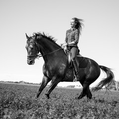 Young happy girl enjoying riding horse on green field at sunny day
