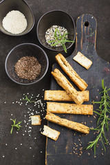 Bread sticks from puff pastry with flax seeds, sesame seeds, sea salt and rosemary on a dark background. Top View.