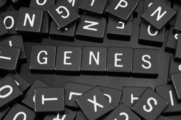 Black letter tiles spelling the word "genes" on a reflective background
