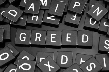 Black letter tiles spelling the word "greed" on a reflective background