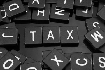 Black letter tiles spelling the word "tax" on a reflective background