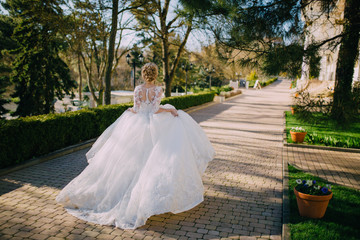 Fototapeta na wymiar A beautiful bride with blond hair running waving her dress on a wedding day. back view