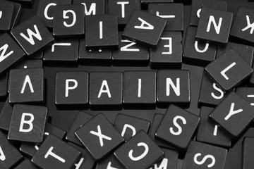 Black letter tiles spelling the word "pain" on a reflective background