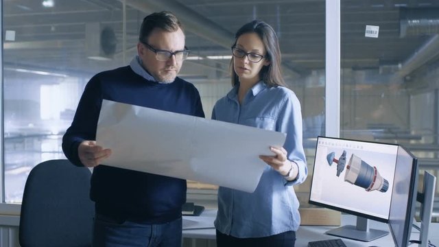 Female Industrial Engineer and Male Chief Engineer Work with Blueprints. Desktop Computer Shows 3D Turbine/ Engine Model. Shot on RED EPIC-W 8K Helium Cinema Camera.