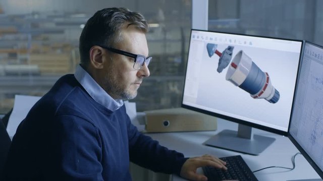 Senior Male Engineer Working on 3D Turbine/ Engine Model on His Computer. In the Background We See Big Factory. Shot on RED EPIC-W 8K Helium Cinema Camera.