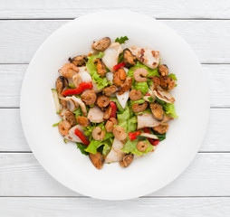 Luxury seafood salad with fresh vegetables. Shrimp, mussels and boiled squid on green lettuce leaf. Healthy food, dietary meal, lunch dish concept. White wooden planks background.