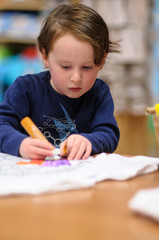 Young boy sitting down at desk indoors coloring with markers