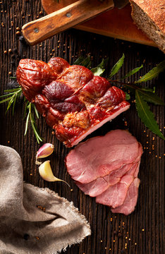 Smoked ham sliced on a wooden rustic table with addition of fresh aromatic herbs, top view.