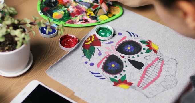 Close-up drawing on clothes. Girl draws on material colorful amazing mexican mask. White T-shirt with pattern. mexican mask. colorful pattern in process. Creative time in the art studio. oilpainting