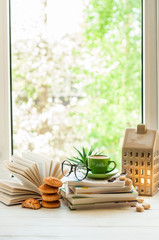 Coffee cup, open book, glasses, cookies and flower on window with bokeh. Reading and breakfast. Concept warm and cozy home decor