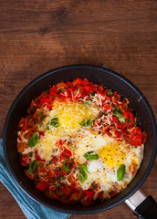 fried eggs with vegetables and cheese in a frying pan on the brown wooden table background. rustic kitchen table with copy space. top view.