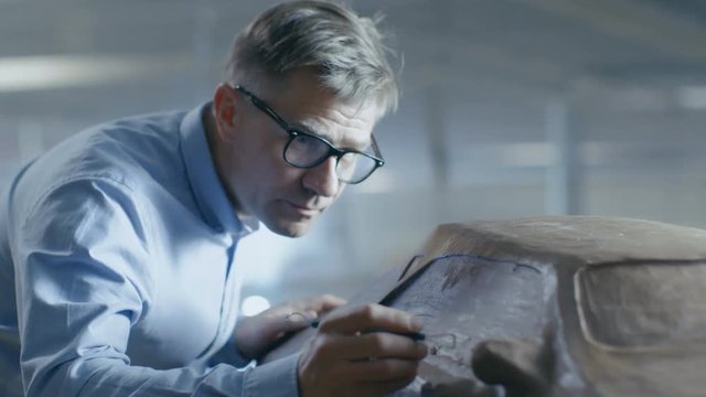 Professional Automotive Designer with Rake Sculpts Futuristic  Car Model from Plasticine Clay. He Works in a Special Studio Located In a Large Car Factory. Shot on RED EPIC-W 8K Helium Cinema Camera.