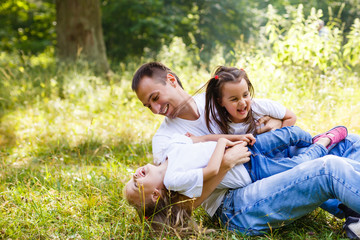 Father with two daughters in white T-shirts sitting and playing on the grass in the park