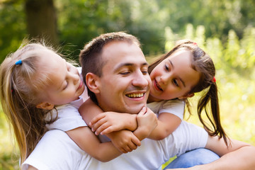 Happy family in outdoor park at sunny day. Dad and two daughters in the green garden. Group of people on green grass.