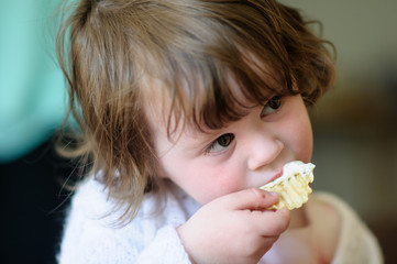 Portrait of a cute little girl inside eating potato chip with sour cream dip on it