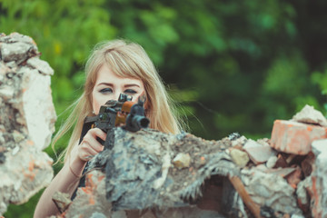 Portrait of a beautiful girl in camouflage in her arms during a war is aiming at a target or an enemy because of shelter