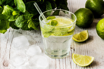 Mojito cocktail with lime, mint and ice on white wooden background.