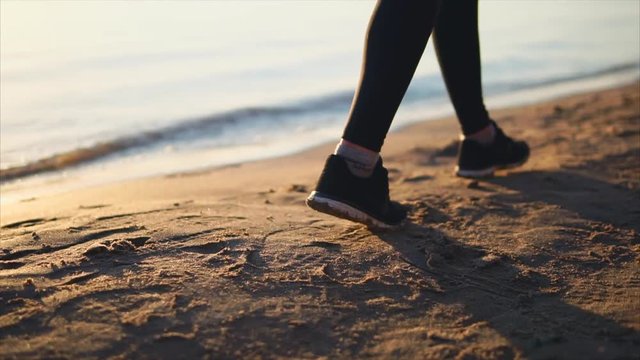 Close up shot of woman legs shod in sneakers walking on the sand beach near the sea.