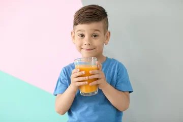 Photo sur Aluminium Jus Mignon petit garçon avec un verre de jus sur fond de couleur