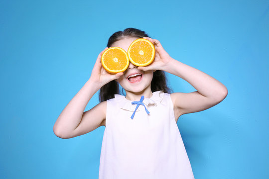 Cute little girl with halves of orange on color background