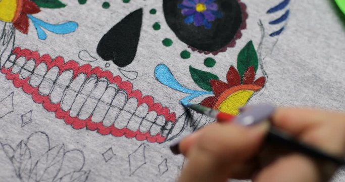 close-up macro shooting drawing colorful mexican mask. young woman's draws on material. woman's hand holding a brush. girl is drawing on clothes. oilpaintig creative time art studio. blue paint color