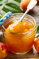 Tasty fruit orange apricot jam in glass jar with fruits on wooden table. Closeup.