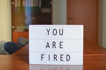 You are fired sign in lightbox put on the desk in office interior. Front view.