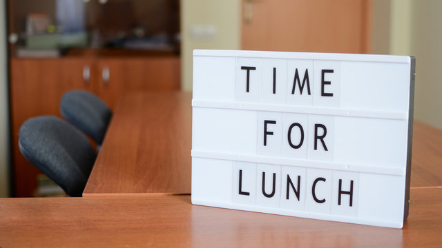 Time for lunch sign in lightbox put on the desk together with hourglass in office interior.