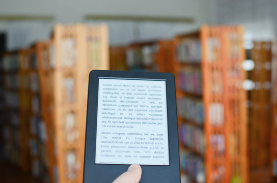 Hand holding ebook reader in classic library with traditional books. Lorem ipsum text used. Concept of technological progress