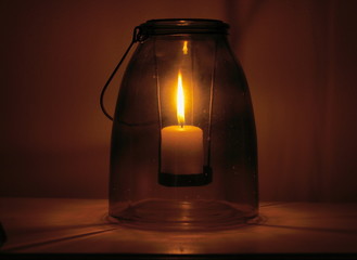 Closeup of a burning candle placed inside an ancient glass recipient.