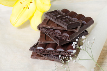 Chocolate bar stacked on a light paper surrounded by flowers. A tower of chocolate cubes