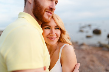 Fototapeta premium Young beautiful smiling couple hugging on the shore amid rocks and sea, enjoy the sunset and freedom. Journey to the sea.