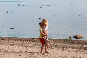 A man picks up the girl on hands. Young beautiful couple hugging with her back to the shore amid...
