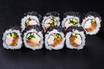 Appetizing delicious fresh sushi roll in black sesame served on black slate, close up.