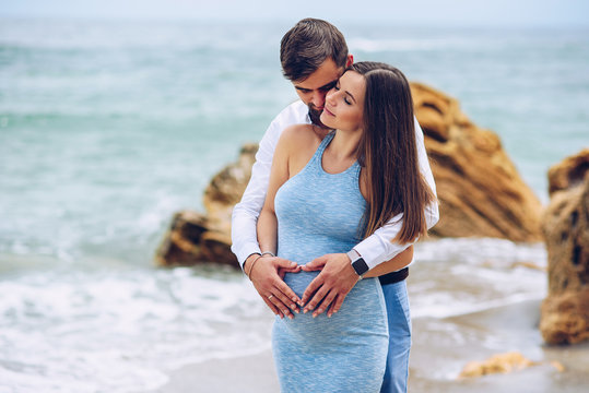 Loving couple making a heart shape on the pregnant belly with their hands.