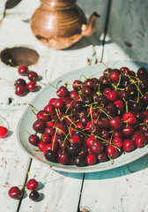 Plate of fresh ripe sweet cherries on rustic light blue wooden garden table, selective focus, vertical composition. Summer food concept