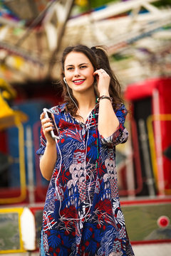 Young woman listening music and holding smart phone in the amusement park