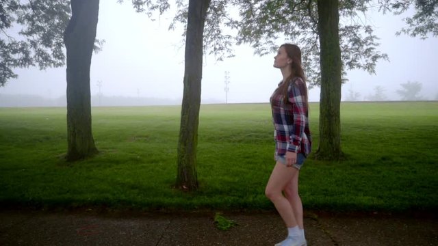 Young woman walking in park. Walking woman in casual dress. Beautiful brunette girl walking in park fog. Profile view of walking girl in park. Alone woman walk at green park