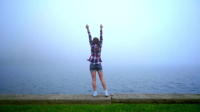 Woman looking out sea. Back view of woman standing on parapet near sea. Dark hair woman dreaming nea sea cost. Dreaming concept. Back view woman looking ocean fog