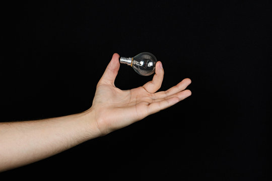 Man's hand holds a light bulb between your fingers isolated on black background