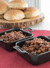 Baked bean and sausage casseroles with buns in background