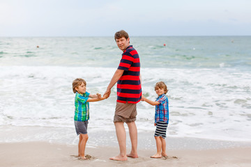 Naklejka premium Two little kids boys and father on the beach of ocean