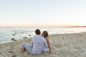 Fototapeta premium Young love couple sitting together on beach, rear view