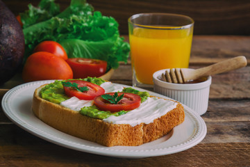 Open sandwich for breakfast or lunch. Healthy sandwich spread with cream cheese,  avocado and tomato.  Avocado and cream cheese open sandwich style serve with orange juice on rustic wood table.