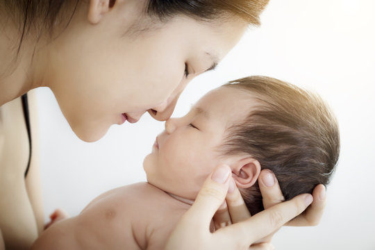 Concept of love and family relationship : Portrait of happy Asian mother use nose touch newborn cute little baby nose on a white bed at home. Parent and little kid relaxing hug and kiss at home.