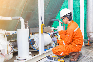 Electrician operator inspect and checking heating ventilated and air conditioning (HVAC), air conditioning service in offshore oil rig platform while worker charging refrigerant in system.