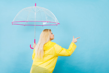 Woman wearing raincoat holding umbrella pointing