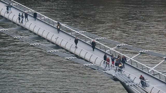 An angled overhead shot of people crossing the Millennium Bridge over the River Thames.