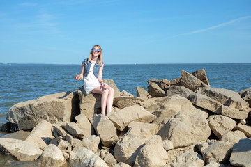 Beautiful young woman sitting on the stone on the seashore